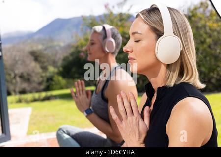 Deux femmes méditant sur des tapis portant des écouteurs après moniteur sur le patio en briques, espace copie Banque D'Images