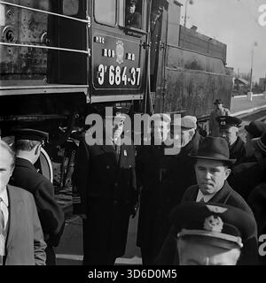 Slavyansk, Ukraine, URSS - années 1970 : photographie d'archives historiques d'un fonctionnaire de haut rang des chemins de fer inspectant la gare. Il se tient sur la plate-forme à côté de la locomotive à vapeur eu 684-37 marquée 'Donetsk Railway' (Don ZH.D.). Le conducteur et son assistant regardent par la fenêtre de la cabine. L'officier est entouré de cheminots et de citoyens. Cette image en noir et blanc capture l'ère de la traction à vapeur et l'importance du transport ferroviaire dans la région industrielle du Donbass. Banque D'Images