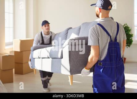 Deux hommes déménageurs transportant le canapé de l'appartement, aidant les gens à se déplacer à un autre lieu de vie Banque D'Images