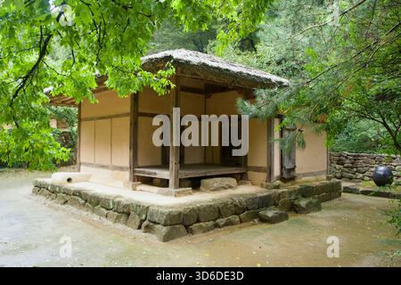 Mungyeong City, Corée du Sud - 28 septembre 2025 : une petite maison traditionnelle au toit de chaume se dresse sur un socle en pierre dans la forêt à côté de l'ancienne route de Mun Banque D'Images
