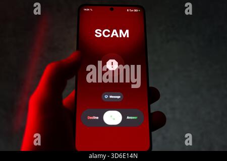 Main tenant smartphone avec avertissement d'arnaque et options d'appel sur écran rouge. Photo de haute qualité Banque D'Images