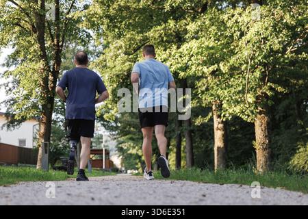 Deux amis masculins font du jogging le long d'un sentier naturel, profitant du plein air tandis que l'un utilise une jambe prothétique. Banque D'Images