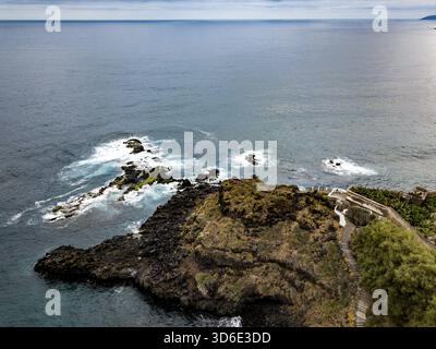Vue aérienne d'un promontoire sombre et rocheux embrassé par des vagues mousseuses où la terre rencontre la vaste mer calme, Tenerife, îles Canaries, Espagne. Banque D'Images