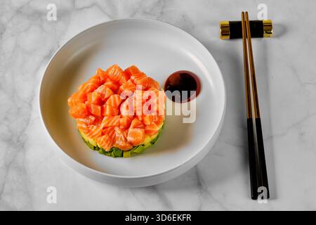 Un plat gastronomique avec un délicat arrangement de saumon coupé en dés sur un lit d'avocat, servi avec un filet de sauce foncée sur une assiette blanche, accompagné Banque D'Images
