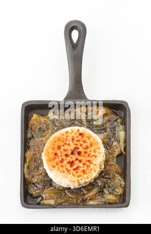 Un délicieux plat avec un rouleau de fromage de chèvre sur un lit d'oignons doux caramélisés, parfaitement disposés dans une poêle rustique en fonte, prêt à servir Banque D'Images