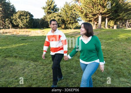 Jeune couple latin se tenant la main et souriant en marchant dans un parc Banque D'Images