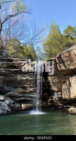 Les chutes d'eau tranquilles de Jackson Falls cascades au-dessus de couches de roche dans une piscine parmi les arbres sous un ciel clair. Banque D'Images