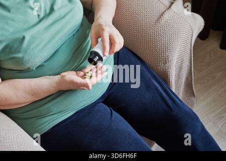 Femme mature versant des capsules vertes de la bouteille dans sa main pour la santé quotidienne Banque D'Images