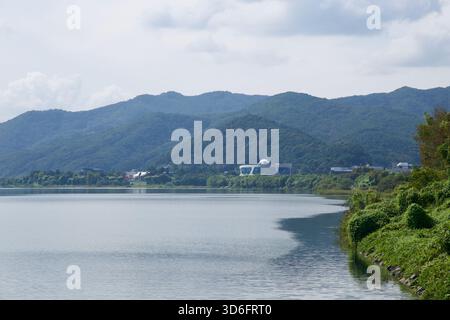 Un bâtiment distinctif en forme de dôme se dresse sur le rivage lointain au-delà de l'eau tranquille du lac Uiam, encadré par des collines verdoyantes et des pentes boisées le long de la rivière North Han Banque D'Images