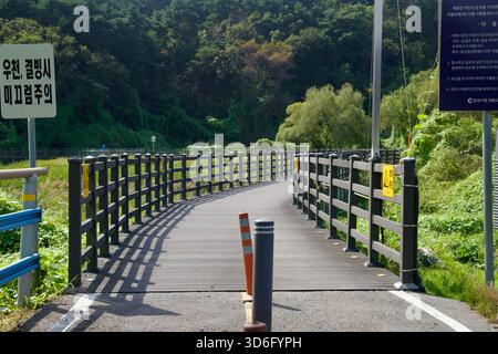 Des panneaux d'avertissement et d'information se dressent à l'entrée d'une promenade en bois de zone humide au bord du lac à Chuncheon, où les balustrades mènent les cyclistes et les marcheurs sur des roseaux Banque D'Images