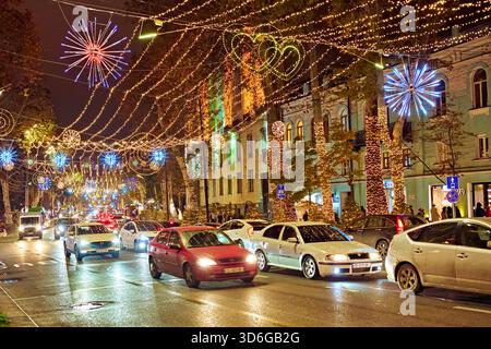 Embouteillage lourd sur une rue urbaine décorée de guirlandes suspendues brillantes et de lumières colorées pendant la nuit de la saison des vacances d'hiver. Banque D'Images