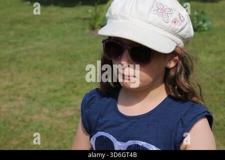 Portrait d'une fille de huit ans portant des lunettes de soleil et chapeau de soleil dans un jardin Surrey Angleterre Banque D'Images