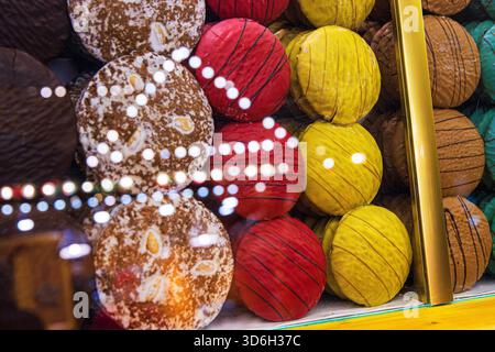 Assortiment de ronds de pain d'épices vibrants décorés à la main en plusieurs couleurs et textures, disposés derrière un comptoir en verre avec réflexion lumineuse festive Banque D'Images