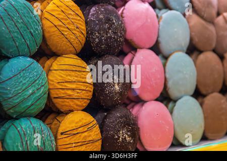 Assortiment de ronds de pain d'épices vibrants décorés à la main en plusieurs couleurs et textures, disposés derrière un comptoir en verre avec réflexion lumineuse festive Banque D'Images