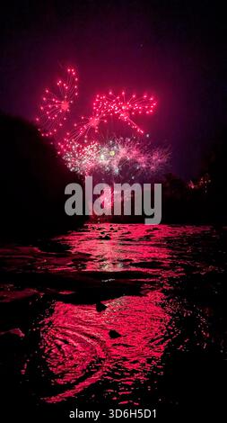 Un feu d'artifice rouge vif illuminant le ciel nocturne pendant Braemar Day, reflété magnifiquement dans les eaux sombres de la rivière Ericht. Banque D'Images
