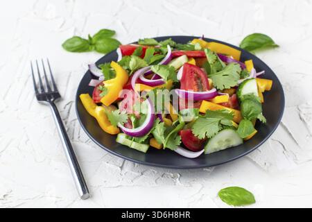 Nourriture, assiette de salade arc-en-ciel avec différents légumes et herbes sur assiette noire avec fourchette sur fond de pierre blanche Banque D'Images