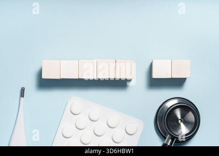 Pose à plat d'articles médicaux, y compris un thermomètre, stéthoscope, blister et blocs de bois sur un fond bleu clair, symbolisant les soins de santé et Banque D'Images