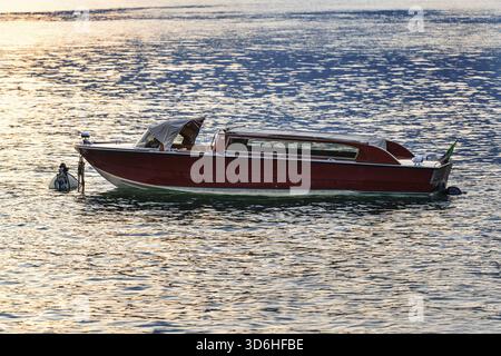 Bateau en bois vintage flotte sur les eaux calmes pendant le coucher du soleil à Varenna, lac de Côme, Italie. La lueur chaude du soleil de décoloration se reflète sur le lac, créant paisible et Banque D'Images