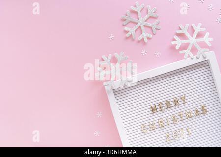 Tableau aux lettres avec voeux joyeux Noël 2021, flocon de neige décoratif sur fond girly pastel rose. Composition de cadre de Noël. Pose à plat, par le dessus Banque D'Images