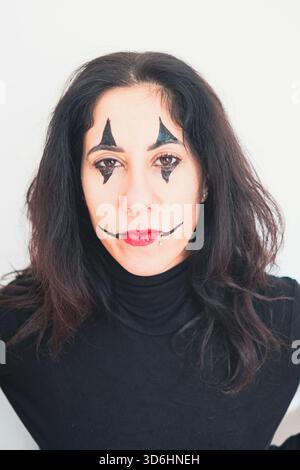 Femme au visage fait pour jouer un clown pour le Carnaval. La femme a trente-huit ans, a de longs cheveux noirs et porte un pull noir à col roulé Banque D'Images