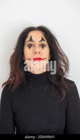 Femme au visage fait pour jouer un clown pour le Carnaval. La femme a trente-huit ans, a de longs cheveux noirs et porte un pull noir à col roulé Banque D'Images