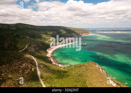 Images de drone montrant Praia do Portinho da Arrabida avec ses eaux turquoises et Convento de Nossa Senhora da Arrabida niché dans les montagnes verdoyantes du parc naturel d'Arrabida, au Portugal Banque D'Images