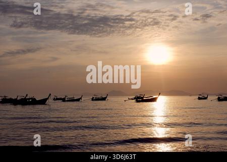 Un large panorama de bateaux sur l'eau plate avec le soleil haut au-dessus de l'océan, soulignant le sentiment d'ouverture, de lumière et de mouvement doux. Banque D'Images