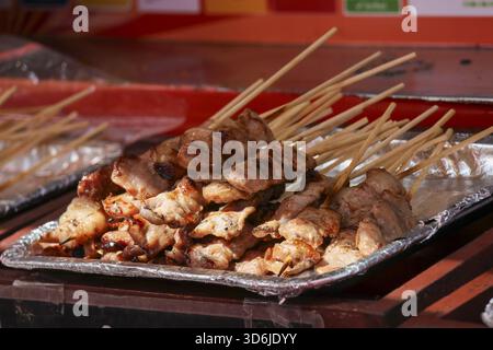 Délicieuses brochettes de poulet grillé sur un plateau en aluminium dans un marché asiatique de Street food. Viande de barbecue appétissante sur bâton, populaire et savoureux traditionnel Banque D'Images