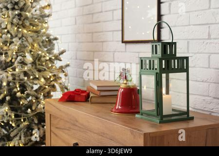 Intérieur du salon avec arbre de Noël, boîte cadeau, livres, cloche et lanterne sur commode près du mur de briques blanches Banque D'Images