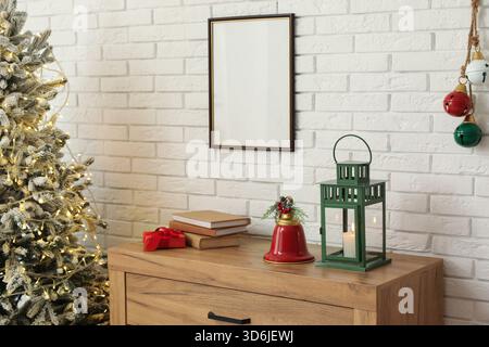 Intérieur du salon avec arbre de Noël, boîte cadeau, livres, cloche et lanterne sur commode près du mur de briques blanches Banque D'Images