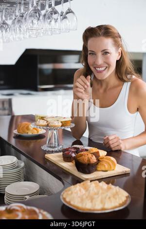 Femme mi-adulte debout derrière le comptoir en bois poli, geste souriant près de cupcakes, espace de copie. Boulangerie, croissant, cupcake, pâtisserie, tarte, image de marque Banque D'Images