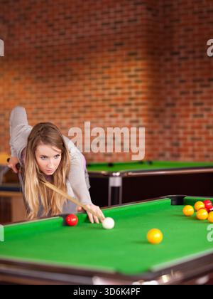 Femme penchée au-dessus d'une table de billard en feutre vert dans le hall, doublée d'une queue près de la boule blanche, espace copie. Billard, gameroom, brique, ambiance, concentrati Banque D'Images