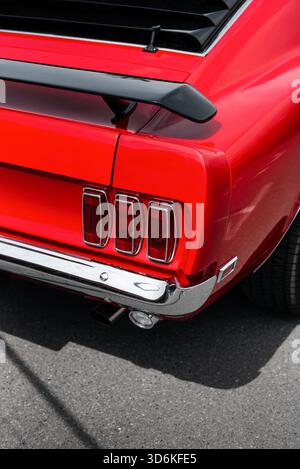 Gros plan arrière de la Mustang 69 rouge : trois feux arrière emblématiques, pare-chocs chromé, aileron arrière noir. Coin arrière droit de la voiture muscle américaine classique. Banque D'Images