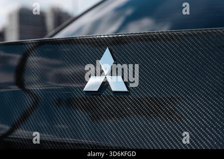 Emblème sur le coffre de la voiture Mitsubishi. Carrosserie de voiture en fibre de carbone brillante avec trois losanges chromés disposés en une formation triangulaire. Banque D'Images