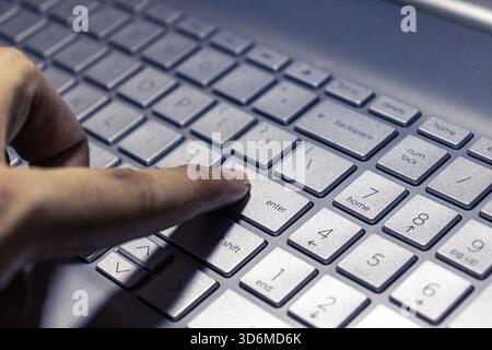 La touche entrée d'un clavier d'ordinateur portable argenté est pressée par un doigt, capturant un moment d'entrée numérique ou d'exécution de commande. Banque D'Images