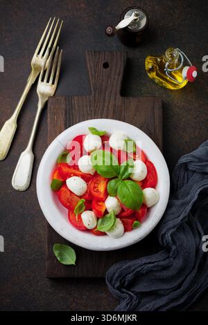 Salade caprese italienne traditionnelle avec tomates, fromage mozzarella et basilic sur fond foncé dans une vieille assiette en céramique blanche. Mise au point sélective.vue de dessus. Copier l'espace. Banque D'Images