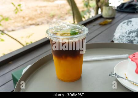 Le thé au citron glacé dans un verre en plastique transparent est servi au client sur la table au café. Banque D'Images