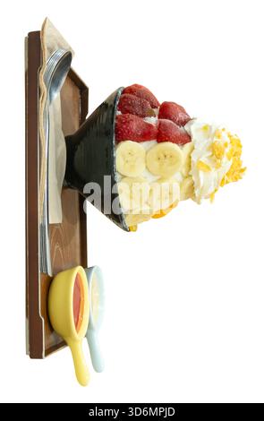 Un ensemble de Bingsu coréen dans un petit bol noir avec plusieurs fruits garniture et sauce rouge avec du lait condensé sucré dans des mini bols en plastique en bois brun Banque D'Images