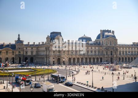 La pyramide du Louvre et les bâtiments du palais environnant à Paris photographiés par un matin clair, avec des visiteurs marchant sur la place et les fontaines. Banque D'Images