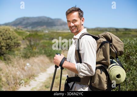 Homme mature debout sur le sentier tenant des bâtons de trekking avec sac à dos et coussin roulé, espace de copie. Randonneur, plein air, nature, paysage, aventure, explorati Banque D'Images