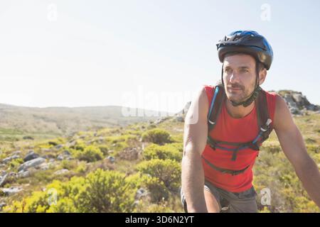 Homme mûr portant débardeur, casque de vélo, s'arrêtant sur un sentier rocheux avec pack d'hydratation, espace de copie. Cycliste, coiffure, robuste, scrubland, aride, landscap Banque D'Images