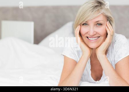 Femme mature s'inclinant sur le lit, souriant, portant le haut de pyjama, montrant la bague, livre de chevet, copier l'espace. Adulte, portrait, détendu, serein, confortable, vêtements de détente Banque D'Images