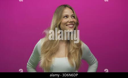 Femme se tient avec les mains sur les hanches dans un cadre de studio photo tout en souriant largement et regardant vers le haut ; confiance joie optimisme positivité. Banque D'Images