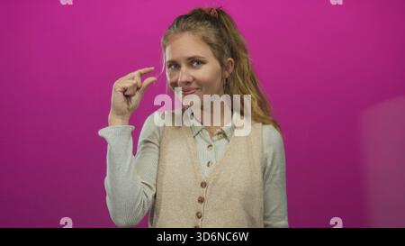 Woman utilise le geste de pincement du doigt dans un studio mettant en vedette jeune influenceur blonde sur un fond rose pour mettre en valeur le design du pull cheveux. Banque D'Images