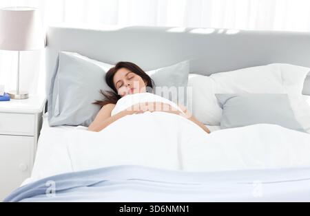 Femme adulte moyenne couchée sur un grand lit dormir dans une chambre avec couette oreillers lampe livre bleu. Literie, tête de lit, rideaux, naturel, léger, pastel, neutr Banque D'Images