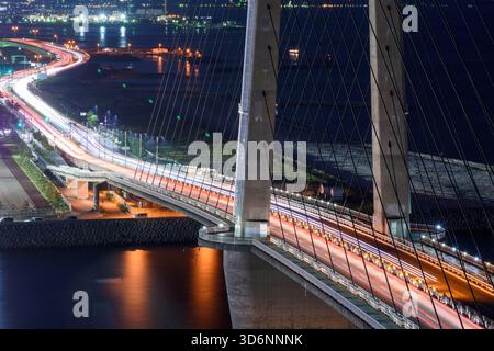 Vue aérienne d'un pont la nuit avec des traînées de lumière provenant de véhicules, lumières de la ville en arrière-plan, eau calme sous-jacente, à Osaka, Japon le 30 septembre 2 Banque D'Images