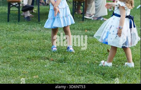 Deux filles dans de belles robes courent sur l'herbe lors d'un festival de ville animé, incarnant la joie et l'esprit de la célébration en plein air Banque D'Images