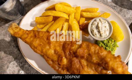Poisson et frites dorés à la bière avec sauce tartare et pois pâteux. Cuisine de pub britannique classique, parfaitement cuisinée et magnifiquement présentée dans un tradit Banque D'Images