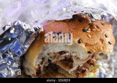 Gros plan sur un hamburger de bœuf en désordre avec bouchée, délicieux plats à emporter pour un déjeuner rapide. délicieux repas pour manger enveloppé dans l'aluminium argenté foi Banque D'Images