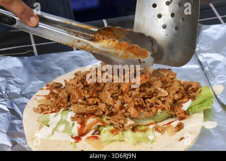Chef préparant un délicieux shawarma kebab wrap. Viande fraîche assaisonnée, laitue et sauce sur pain plat. Cuisine de rue savoureuse exposée dans un Outdoo Banque D'Images